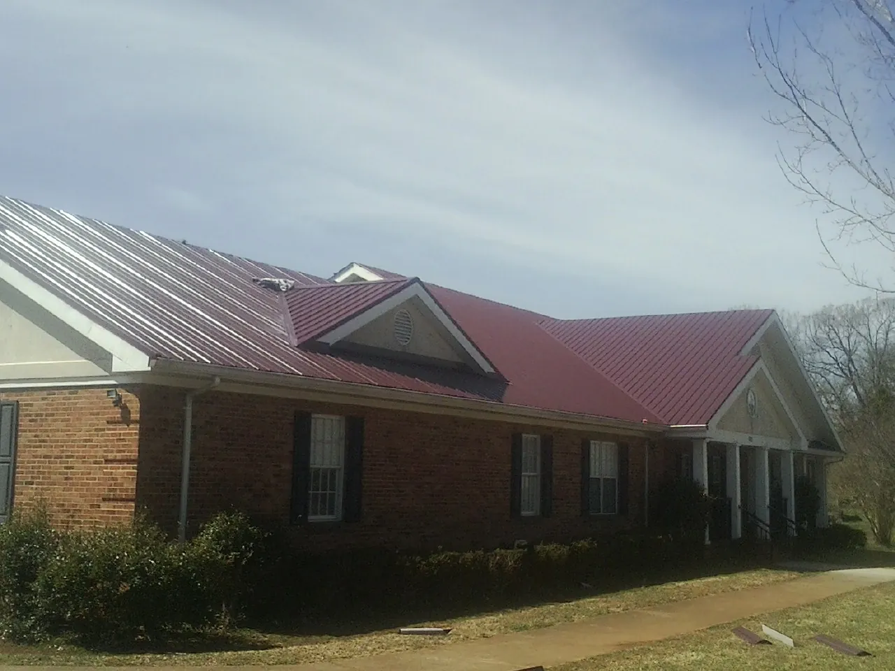 Red metal roof with gabled entries on a long brick building, from a Hail Damage Roof Repair job in Big Bear Lake