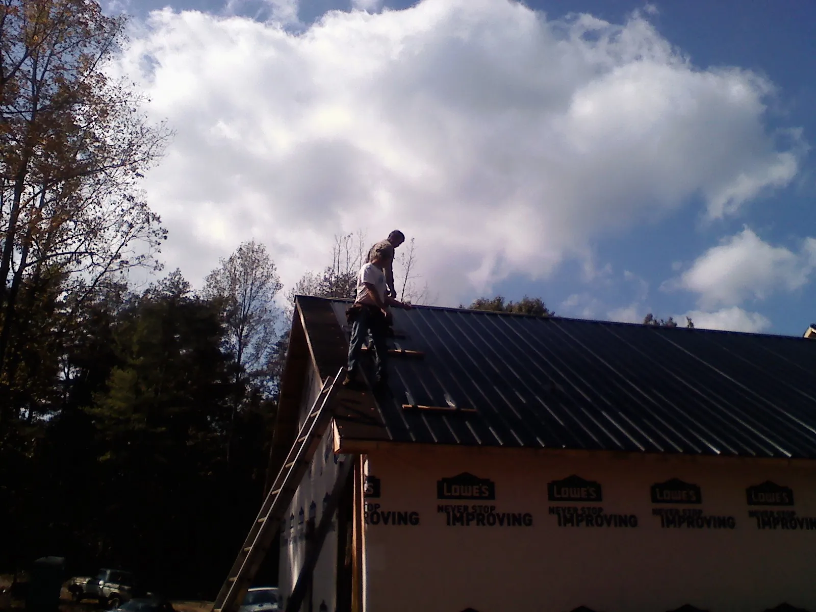 Roofer fastening dark metal panels high against a cloudy sky, from a Roof Inspection job in Big Bear Lake